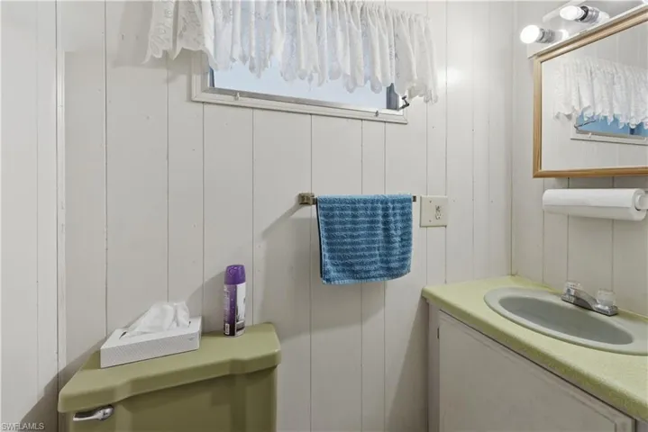 Bathroom featuring vertical paneled walls, a single window with curtain, an oval sink with a laminate countertop, and a wall-mounted mirror