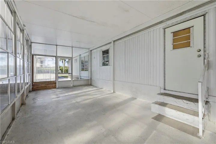 Screened lanai featuring concrete flooring, a white metal frame, and an entry door with a privacy window