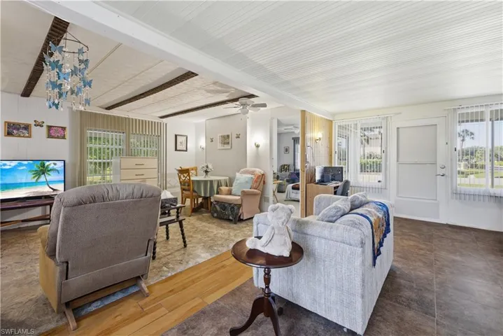 Spacious interior featuring a combination of wood-finish and tile flooring, vertical window blinds, a built-in ceiling fan, and exposed ceiling beams