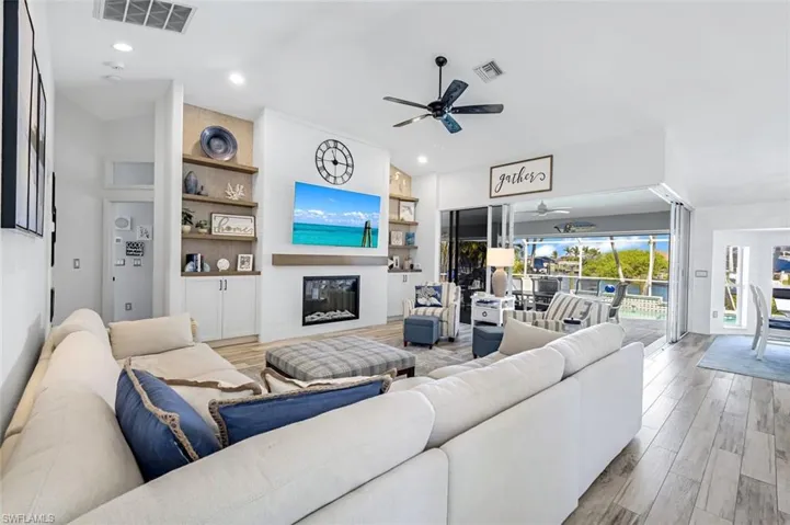 Living room with a fireplace, wood finished floors, visible vents, and a ceiling fan