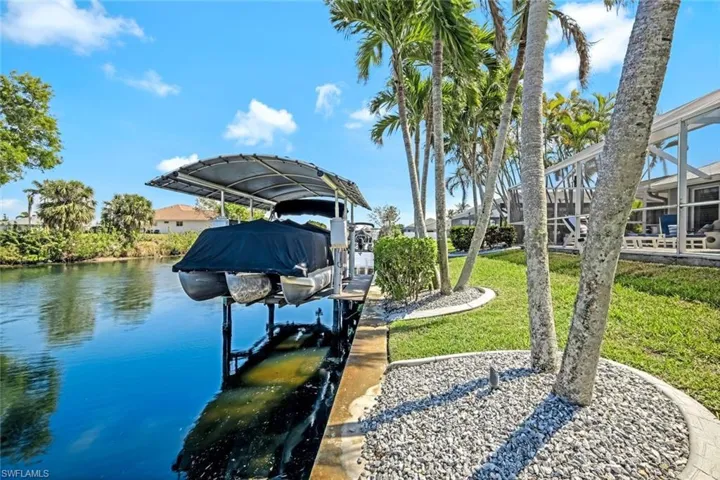 View of dock with a lanai, a water view, boat lift, and a lawn