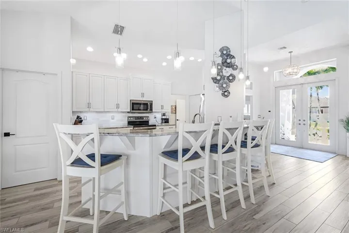 Kitchen with decorative backsplash, appliances with stainless steel finishes, french doors, light wood-style floors, and white cabinetry