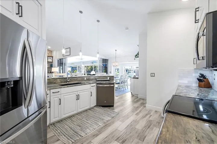 Kitchen featuring decorative backsplash, appliances with stainless steel finishes, light wood-style floors, white cabinetry, and a sink