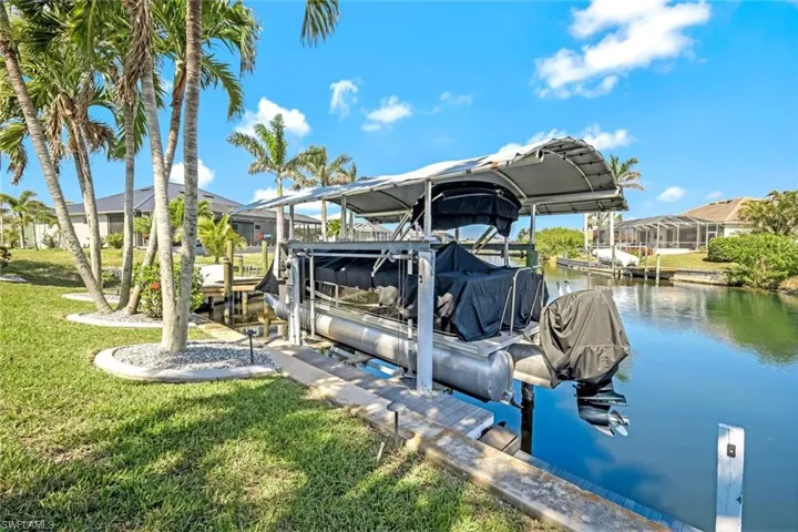 View of dock with a water view, boat lift, a residential view, and a lawn