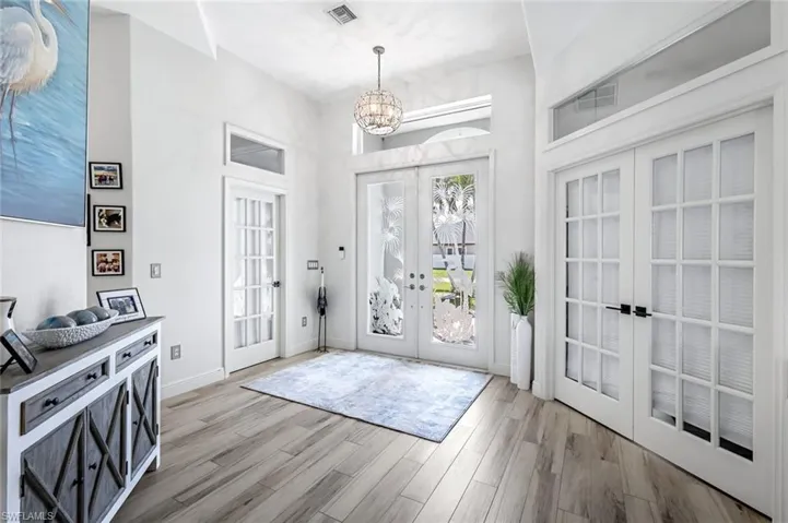 Foyer entrance featuring visible vents, baseboards, french doors, light wood finished floors, and an inviting chandelier