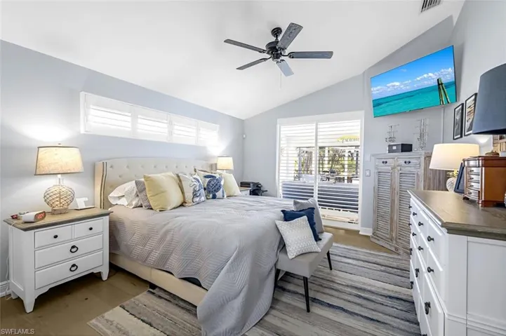 Bedroom with light wood finished floors, visible vents, a ceiling fan, vaulted ceiling, and access to outside