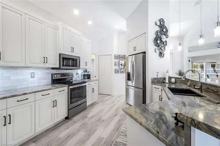 Kitchen featuring tasteful backsplash, dark stone counters, stainless steel appliances, white cabinetry, and a sink