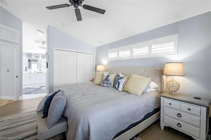 Bedroom featuring a ceiling fan, ensuite bath, wood finished floors, vaulted ceiling, and a closet