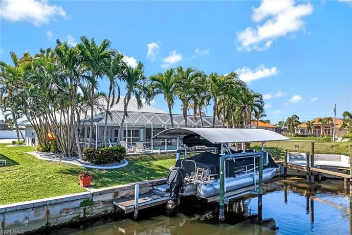 View of dock featuring a lanai, a water view, boat lift, and a yard