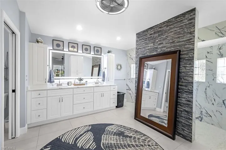 Full bath featuring tile patterned floors, a sink, a marble finish shower, and double vanity