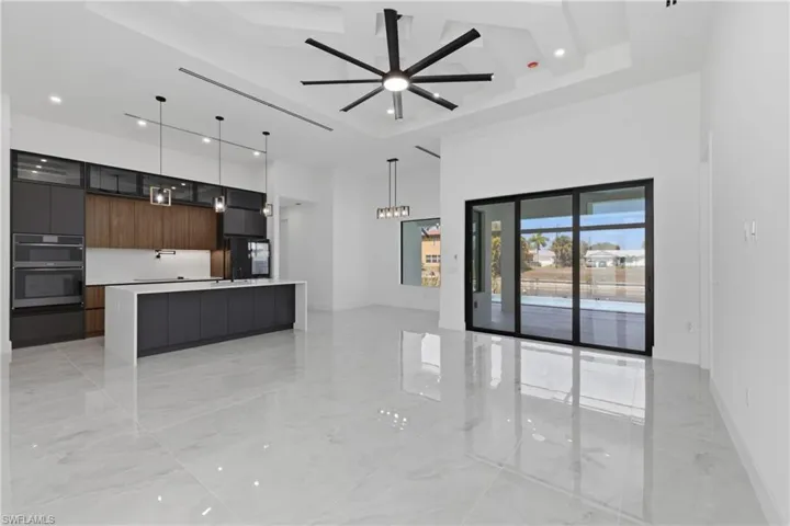 Unfurnished living room with a tray ceiling, ceiling fan, recessed lighting, and light marble finish floors