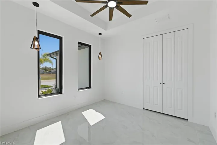Unfurnished bedroom with light marble finish floors, a ceiling fan, a tray ceiling, and a closet