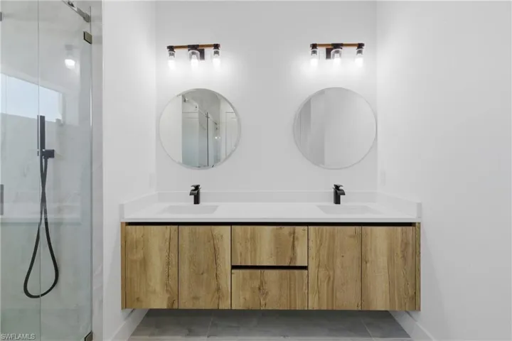 Bathroom featuring double vanity, a marble finish shower, and tile patterned floors