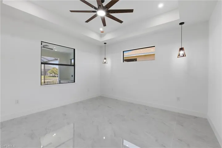 Unfurnished room featuring a tray ceiling, recessed lighting, light marble finish floors, and a ceiling fan