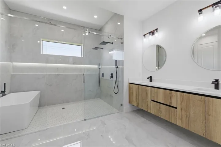 Full bath with double vanity, a marble finish shower, and a freestanding bath