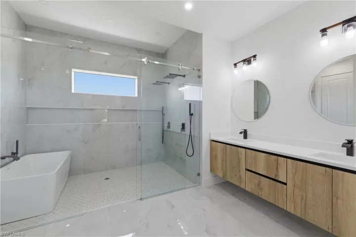 Bathroom featuring double vanity, a marble finish shower, and a freestanding tub
