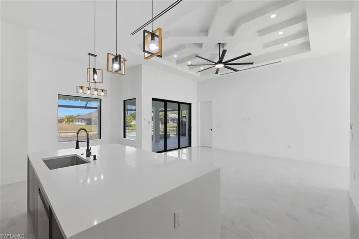 Kitchen featuring coffered ceiling, an island with sink, hanging light fixtures, open floor plan, and light stone countertops