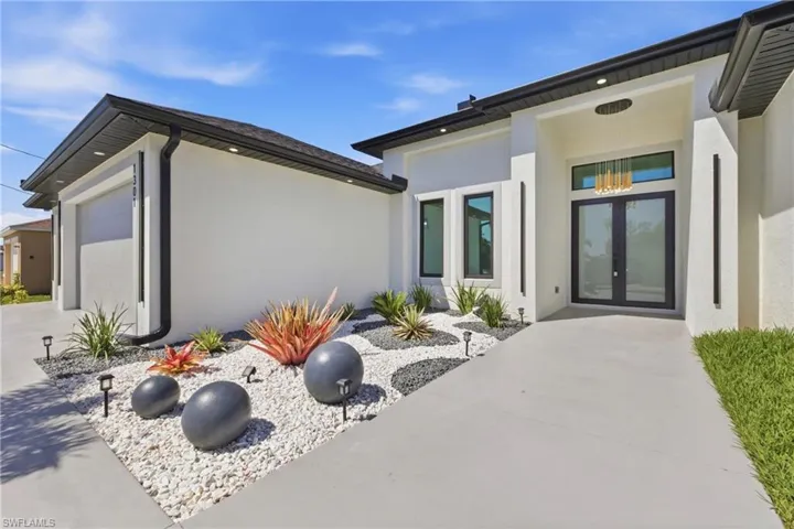 Property entrance with french doors, stucco siding, an attached garage, and concrete driveway