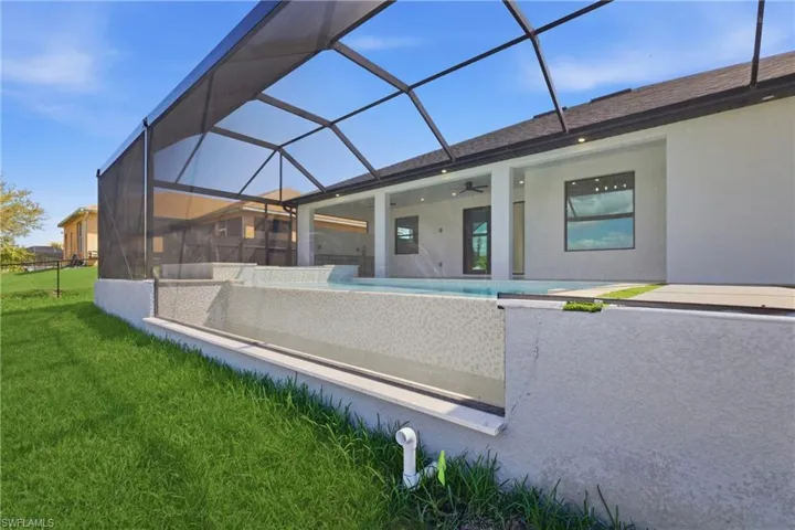 Back of house with a sunroom, a lanai, a ceiling fan, a lawn, and an outdoor pool