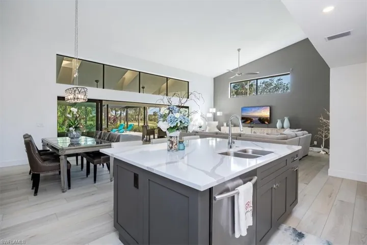 Kitchen featuring sink, hanging light fixtures, light stone counters, light hardwood / wood-style floors, and ceiling fan with notable chandelier