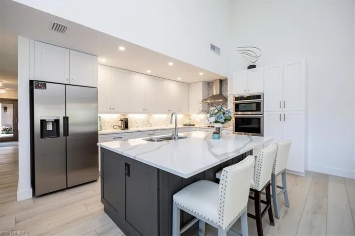 Kitchen featuring appliances with stainless steel finishes, wall chimney exhaust hood, sink, a center island with sink, and white cabinetry