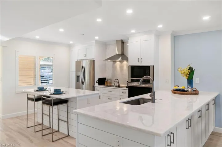 Kitchen featuring white cabinetry, wall chimney exhaust hood, a large island, and appliances with stainless steel finishes