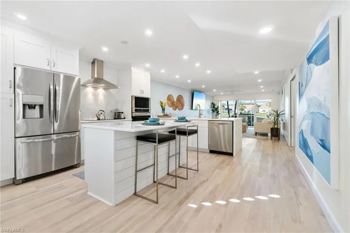 Kitchen featuring wall chimney exhaust hood, Frigidaire Gallery Appliances, a breakfast bar, stainless steel appliances, white shaker cabinets, and a kitchen island with white marble.