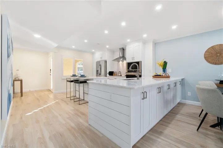 Kitchen featuring kitchen peninsula, stainless steel refrigerator with ice dispenser, sink, wall chimney range hood, and white cabinetry