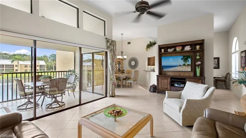 Living room featuring ceiling fan, hanging lights, light tile patterned floors, and a high ceiling
