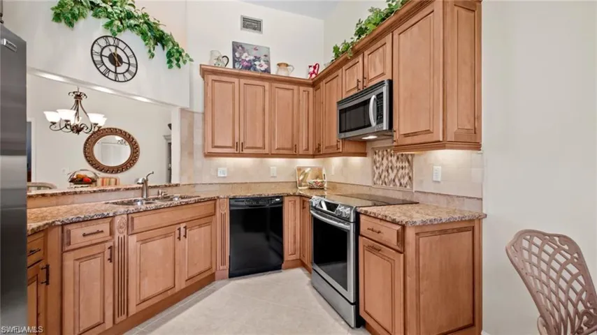 Kitchen featuring stainless steel appliances, light stone counters, backsplash, a chandelier, and light tile patterned floors