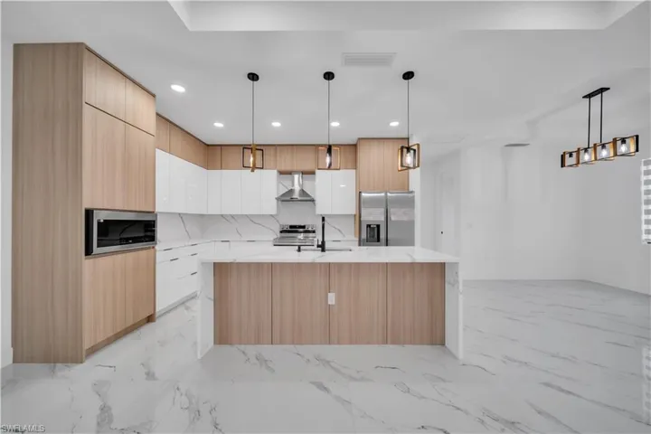 Two tone kitchen featuring light stone counters, modern cabinets, a kitchen island with sink, stainless steel appliances, and decorative backsplash