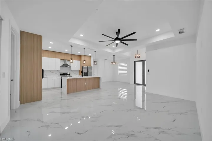 Kitchen featuring open floor plan, modern cabinets, an island with sink, a ceiling fan, and stainless steel appliances