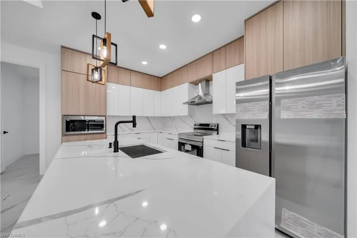 Kitchen with stainless steel appliances, light stone counters, a kitchen island with sink, and light wood finish cabinetry