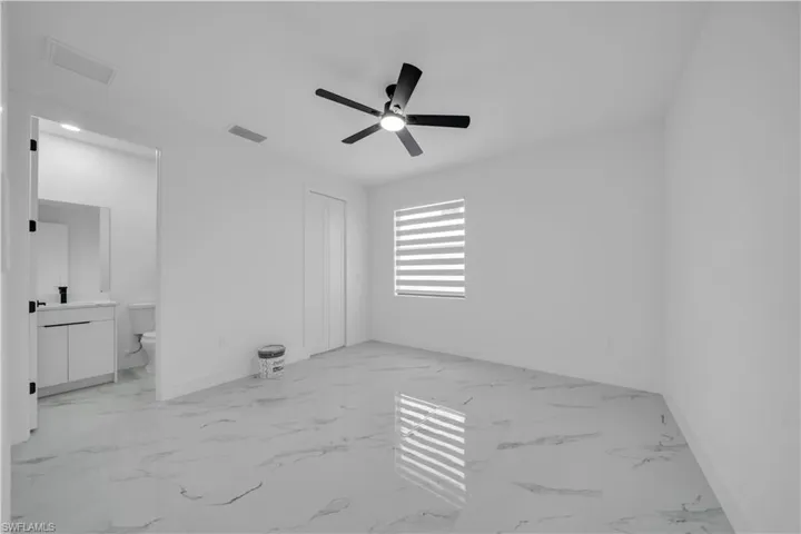 Unfurnished bedroom featuring a ceiling fan, a closet, light marble finish floors, and connected bathroom