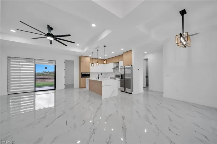 Kitchen featuring open floor plan, an island with sink, modern cabinets, decorative light fixtures, and stainless steel appliances