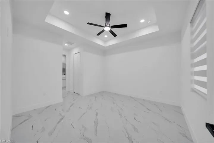 Unfurnished room featuring recessed lighting, ceiling fan, a tray ceiling, and light marble finish floors