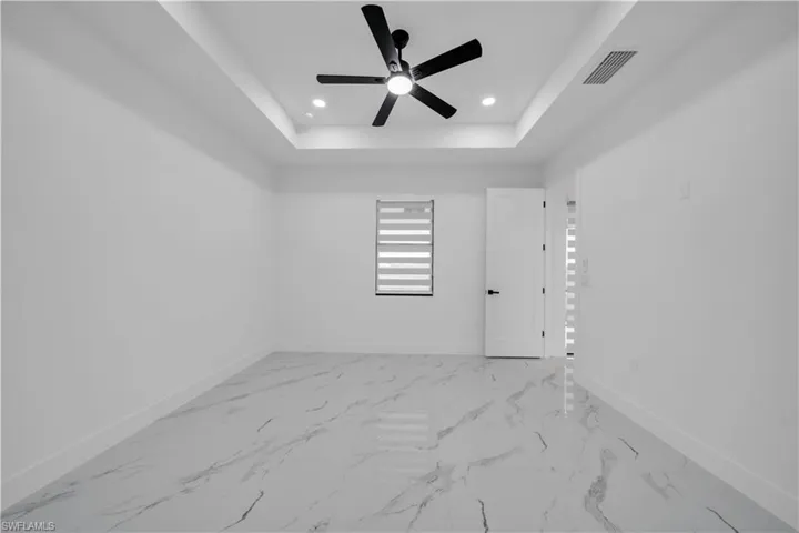 Unfurnished room with a ceiling fan, recessed lighting, light marble finish flooring, and a tray ceiling