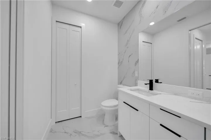Bathroom with a closet, vanity, recessed lighting, stone wall, and light marble finish floors