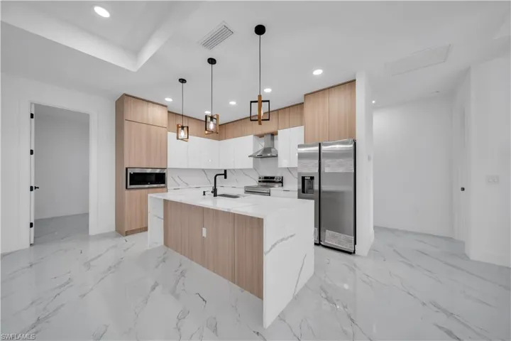 Dual tone kitchen with light stone counters, a center island with sink, stainless steel appliances, modern cabinets, and pendant lighting