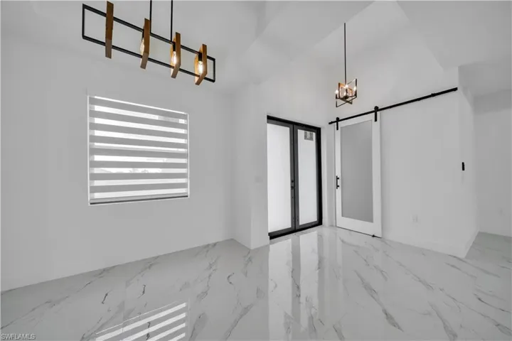 Unfurnished dining area with a barn door, hanging lights, light marble finish flooring, vaulted ceiling, and french doors