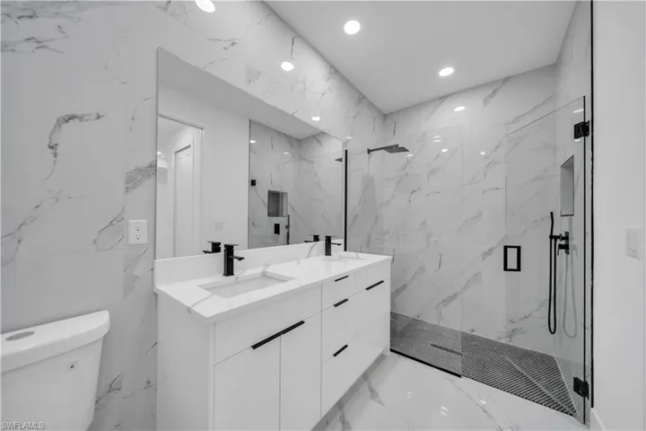 Full bathroom with stone wall, double vanity, a marble finish shower, and recessed lighting