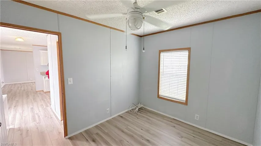 Empty room featuring a textured ceiling, light wood-type flooring, and ceiling fan