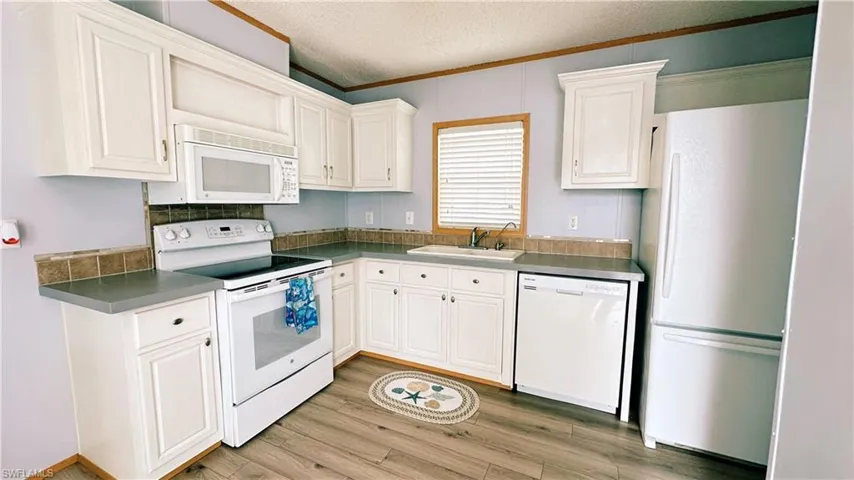 Kitchen with sink, light wood-type flooring, white cabinetry, and white appliances