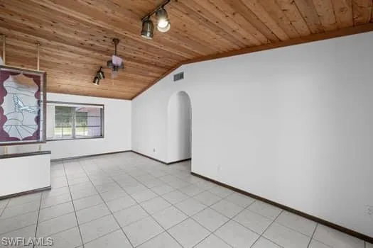 Unfurnished room with wooden ceiling, arched walkways, rail lighting, vaulted ceiling, and light tile patterned flooring