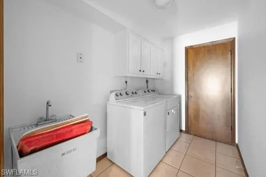 Laundry area with light tile patterned floors, washing machine and dryer, and cabinet space