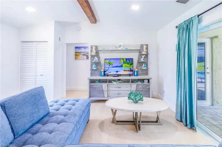 Living area featuring high vaulted ceilings with a wood beam accent, tile flooring, and a sliding glass door providing access to an outdoor patio with a visible pool