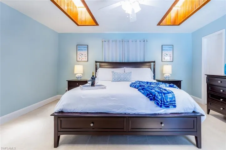 Bedroom featuring a light blue wall color, tray ceiling with wood-finish accents, a ceiling fan, and light-toned flooring