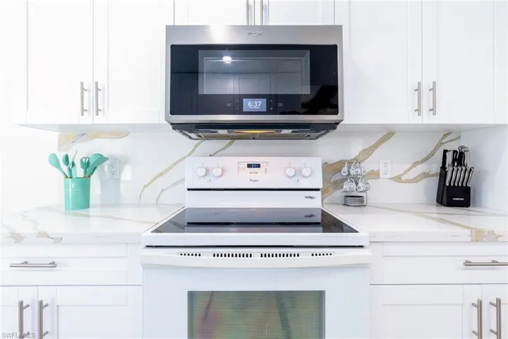 Contemporary kitchen featuring white cabinetry with brushed nickel hardware, a stainless steel over-the-range microwave, and a white electric range