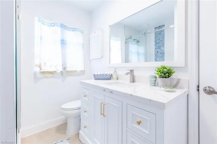 White vanity with gold-finish hardware, a rectangular undermount sink, and a stone-finish countertop