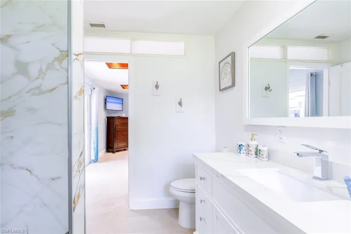 Bright bathroom featuring a large vanity with dual integrated sinks, chrome fixtures, and a spacious framed mirror